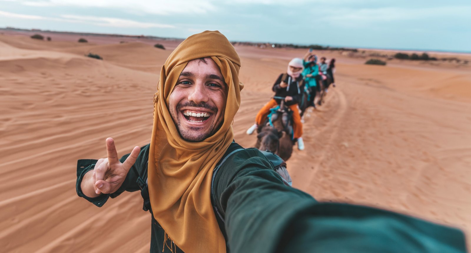 Amidst the rolling dunes, a moment of pure elation is captured as a man shares his expedition with the world through a selfie. His cheerful demeanor and the casual camaraderie of the group on camelback reflect a journey that's as much about the shared experience as it is about the destination. It's an invitation to immerse oneself in the cultural and adventurous offerings of the desert.