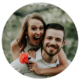 This heartwarming image features a couple sharing a lighthearted, joyful moment together. The woman's exuberant expression, as she playfully grasps a vibrant orange flower, complements the man's contented smile, creating a picture of genuine happiness and affection. Framed by the soft focus of the surrounding greenery, the couple's connection is the clear focal point, embodying a spontaneous celebration of love.